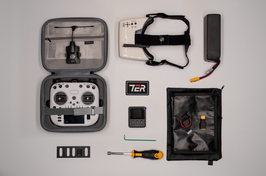 A drone accessory kit laid out on a light gray background, including an open hard case with a white controller inside, a white headset, a black rectangular battery or power unit, a black zip pouch with small accessories, a black patch reading TCR, a small black device, screws, and tools.