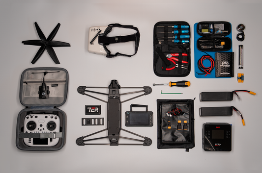 A complete drone repair and flying kit laid out neatly on a light gray background, including a drone frame, propellers, a remote controller in an open zip case, batteries, a headband, a tool organizer with screwdrivers, and various small repair tools.