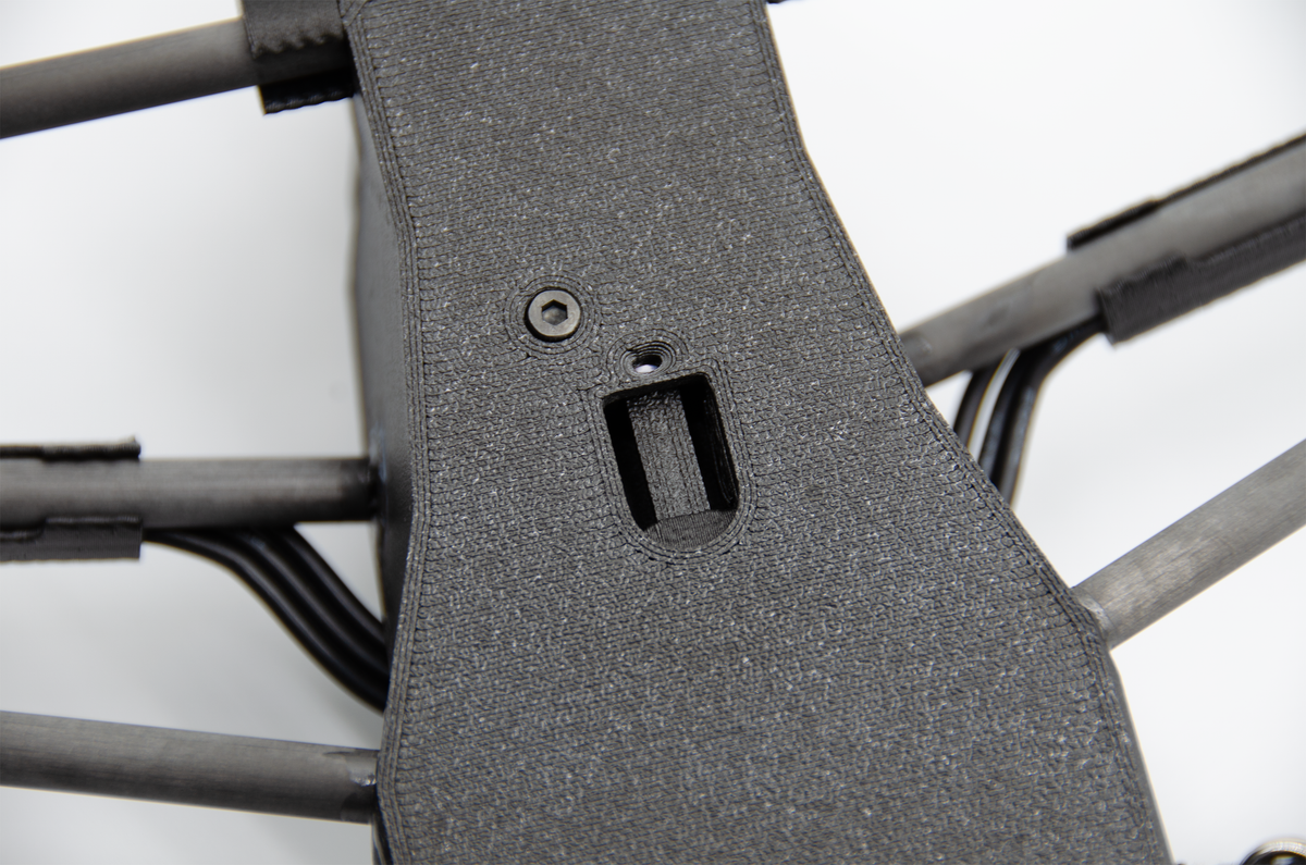 Close-up of a dark gray textured protective cover or panel mounted on the frame of a quadcopter drone, showing a screw and a mounting slot.