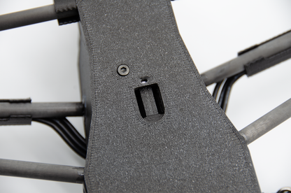 Close-up of a dark gray textured protective cover or panel mounted on the frame of a quadcopter drone, showing a screw and a mounting slot.