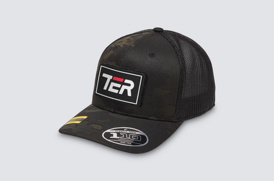 A black trucker hat with a dark camouflage pattern on the front panels and visor, featuring a white rectangular patch with 'TER' in white and red on the front, and a silver '110' sticker on the brim.