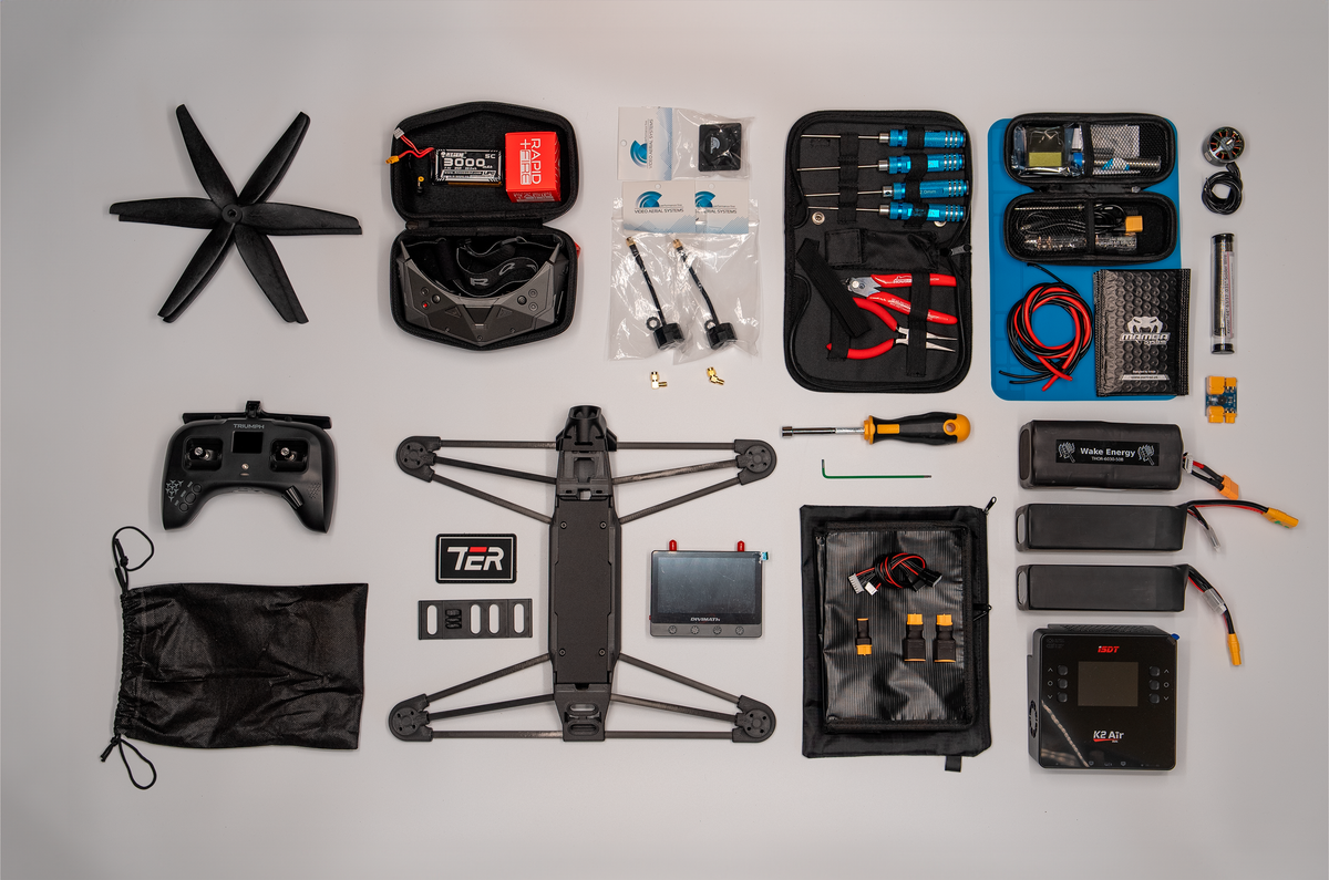A complete drone kit laid out neatly on a light gray background, including a black quadcopter drone, propellers, FPV controller, batteries, tools, and accessories in carrying cases.