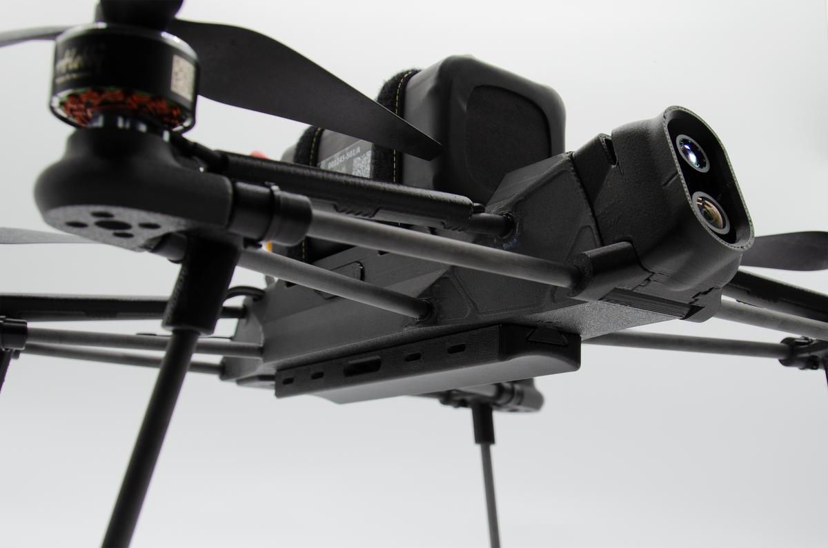 Close-up of a black quadcopter drone with a mounted camera and propellers against a light gray background.