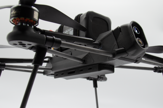Close-up of a black quadcopter drone with a mounted camera and propellers against a light gray background.