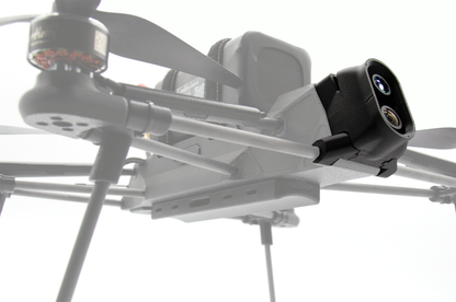 A close-up of a gray quadcopter drone with a black camera mount attached to the side, photographed against a bright white background.