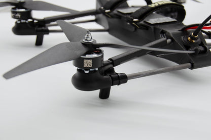 Close-up of a black quadcopter drone with dark gray propellers, showing the motor, landing gear, and part of the fuselage on a white background.