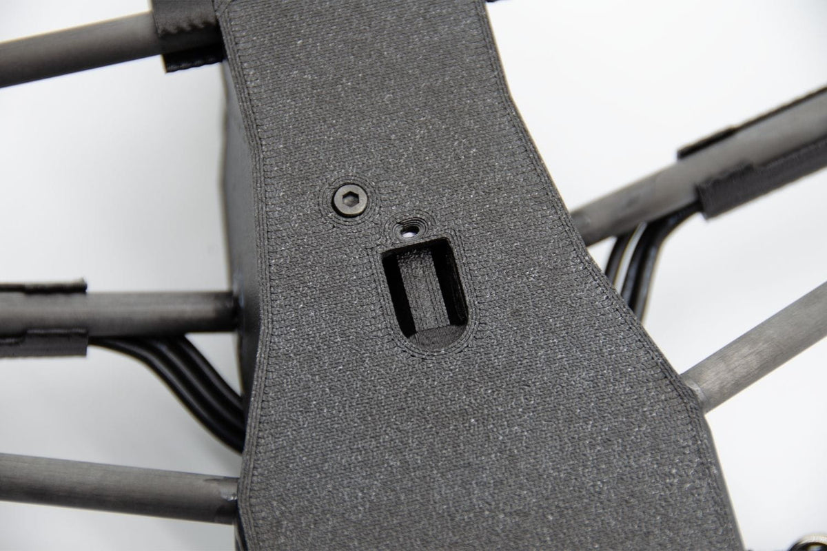 Close-up of a dark gray textured protective cover or panel mounted on the frame of a quadcopter drone, showing a screw and a mounting slot.