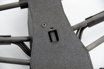 Close-up of a dark gray textured protective cover or panel mounted on the frame of a quadcopter drone, showing a screw and a mounting slot.