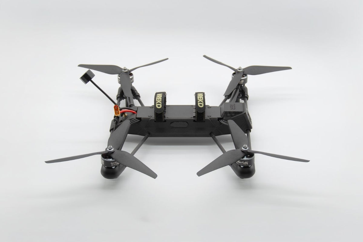 A black quadcopter drone with four propellers, shown from a top-down perspective on a light gray studio background.