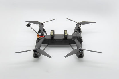 A black quadcopter drone with four propellers, shown from a top-down perspective on a light gray studio background.