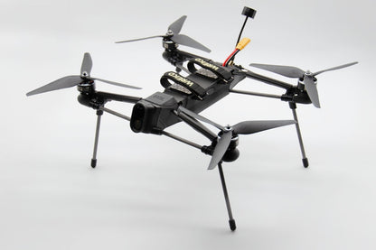 A black quadcopter drone with four propellers, landing legs, and a mounted camera, photographed on a clean light gray studio background.
