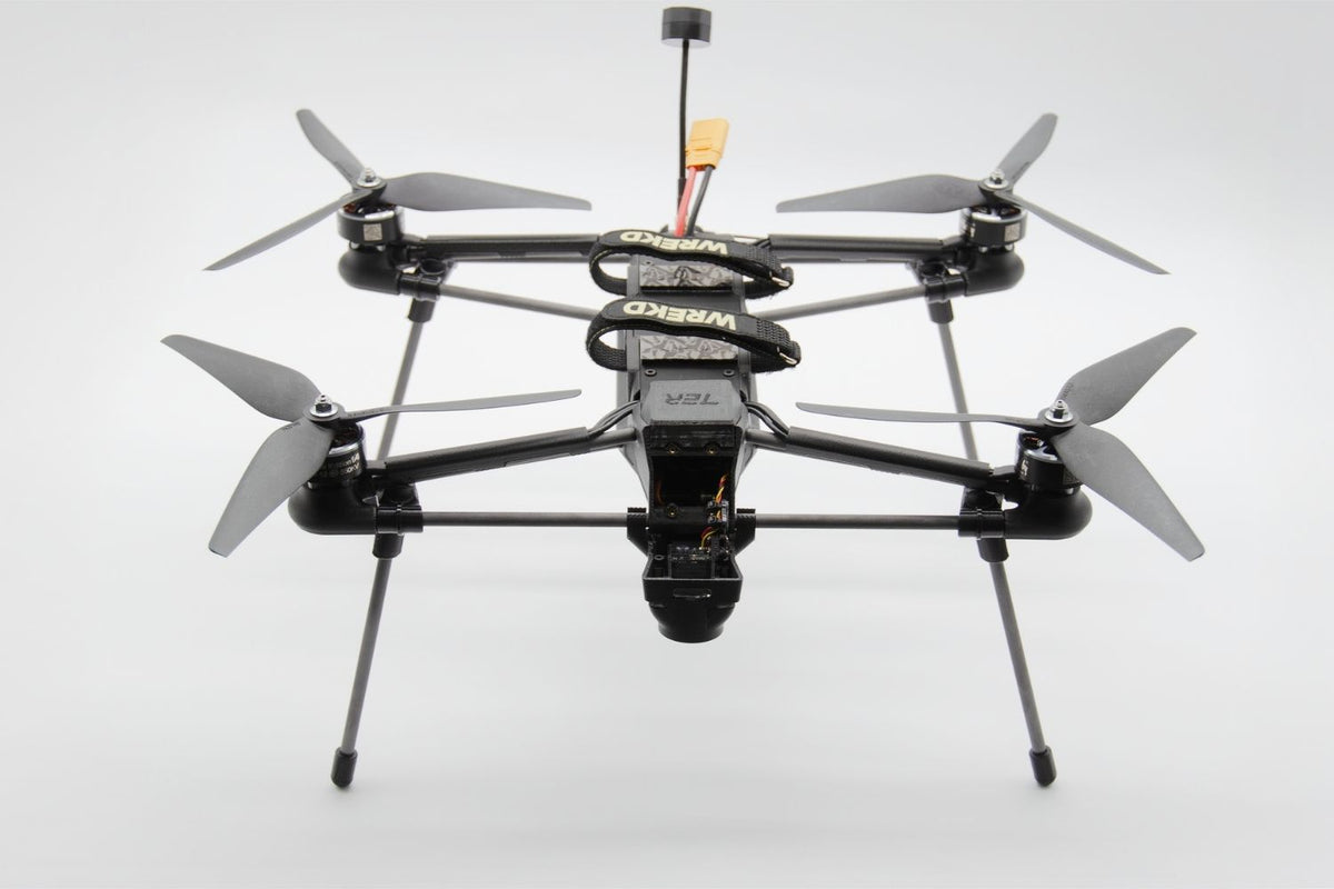 A black quadcopter drone with a mounted camera, four propellers, and landing legs, photographed against a seamless light gray background.