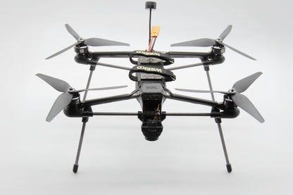 A black quadcopter drone with a mounted camera, four propellers, and landing legs, photographed against a seamless light gray background.