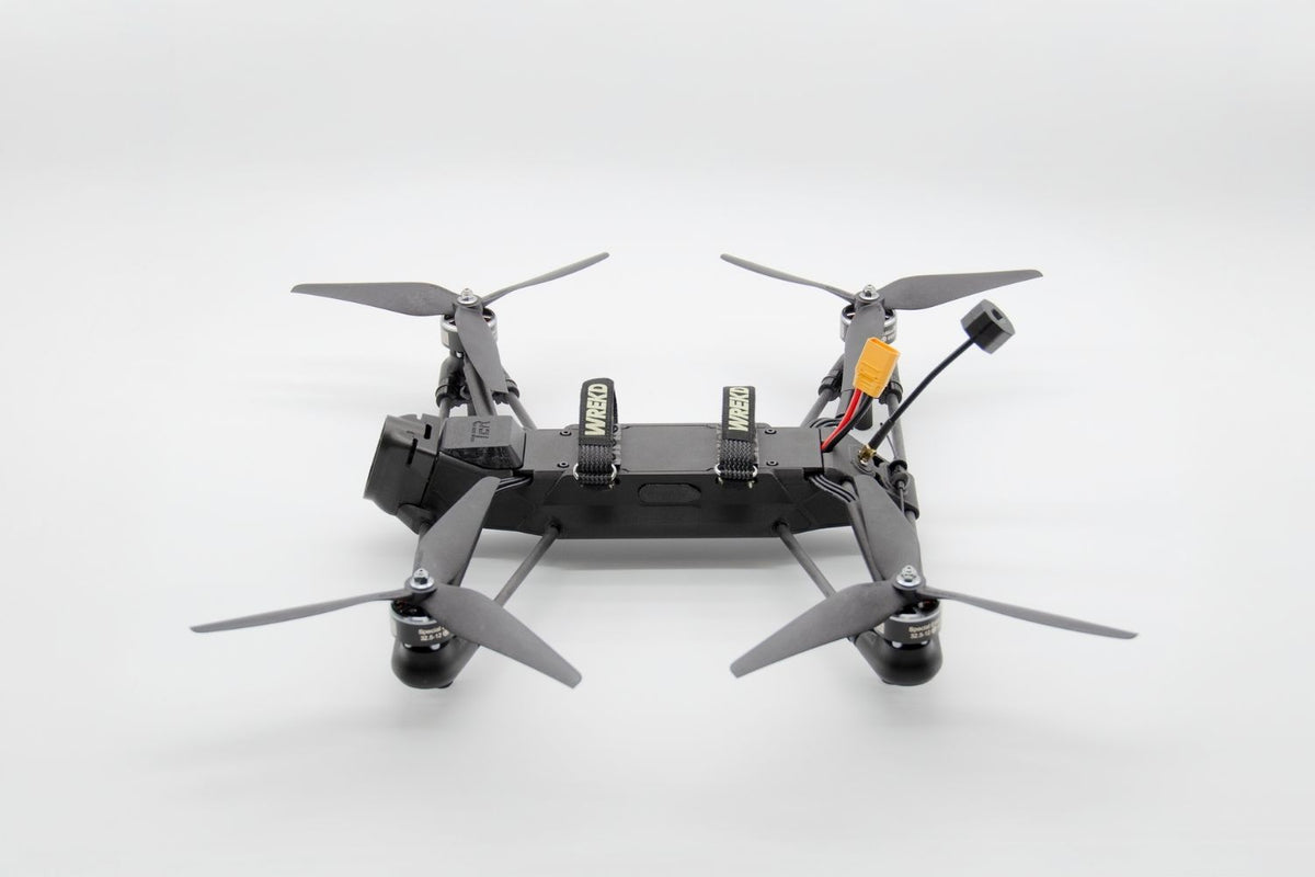A black quadcopter drone with four gray propellers, a mounted camera, and visible battery packs on a clean white studio background.