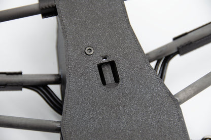 Close-up of a dark gray textured protective cover or panel mounted on the frame of a quadcopter drone, showing a screw and a mounting slot.
