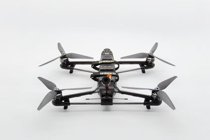 A black quadcopter drone with four gray propellers, featuring a camera lens on the front and visible 'WREKD' branding, photographed from a top-down angle on a white background.