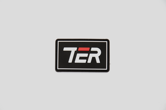 A rectangular black patch with a white border and the stylized letters 'TER' in white, featuring a red accent bar over the middle letter, shown on a light gray background.