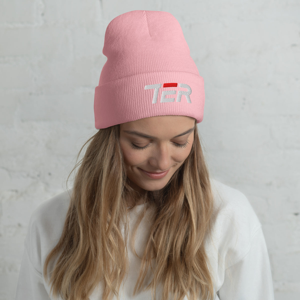 Woman wearing a pink beanie with 'TER' embroidery against a light gray background
