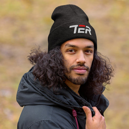 Man wearing a dark grey beanie with a TER logo and a black jacket outdoors.