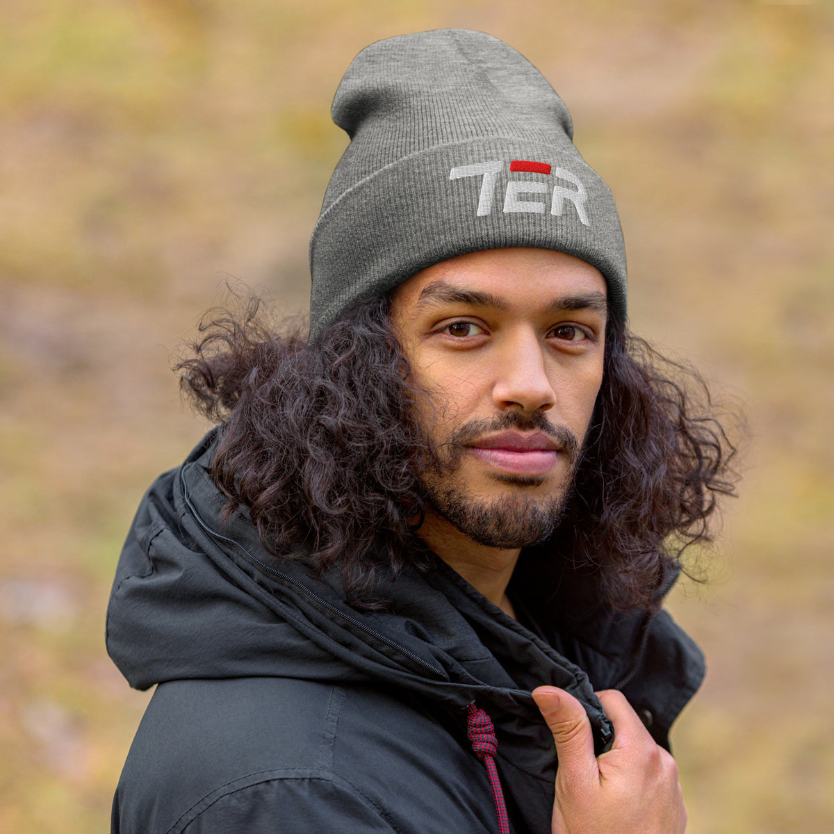 Man wearing a gray beanie with a logo and a black jacket outdoors.